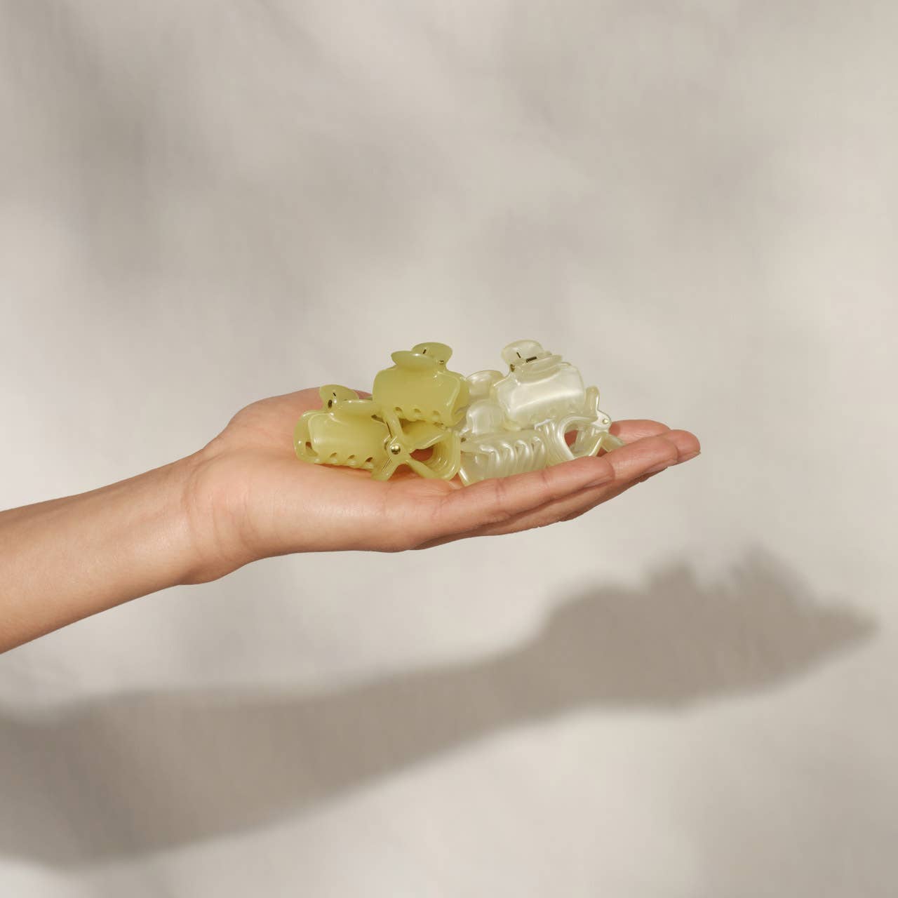 Hand holding a clear  and yellow KITSCHclaw clips object against a plain background