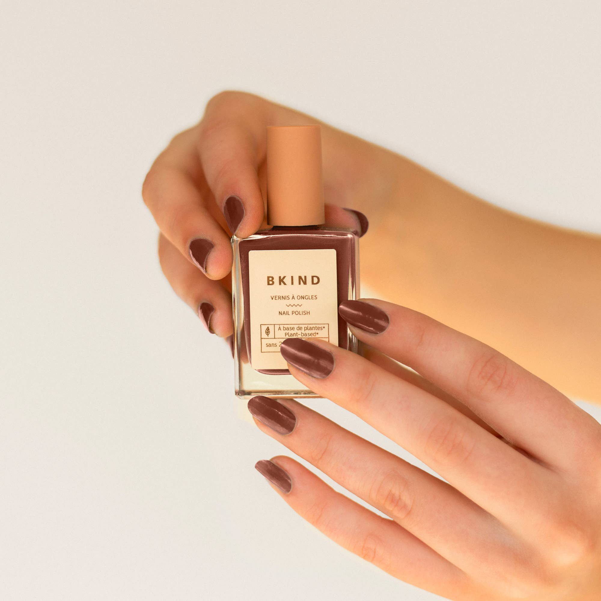 Hand holding a bottle of BKIND nail polish with a neutral background