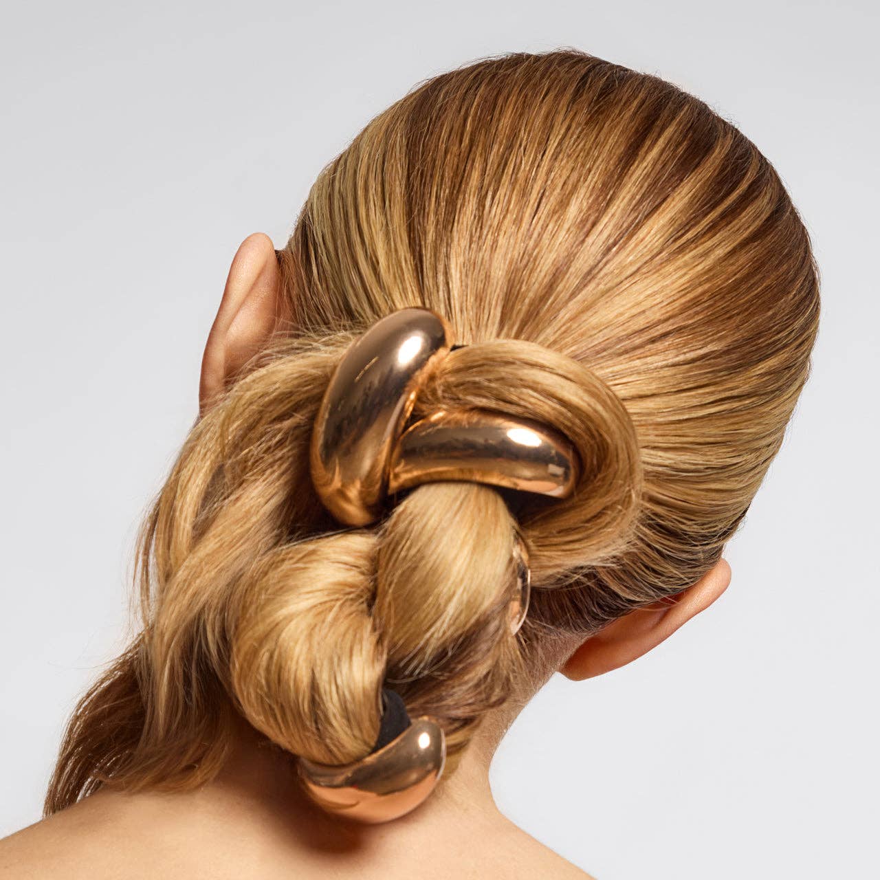 Gold hair accessory in a styled bun on a neutral background. Kitsch gold metal cloud cuff ponitail holder