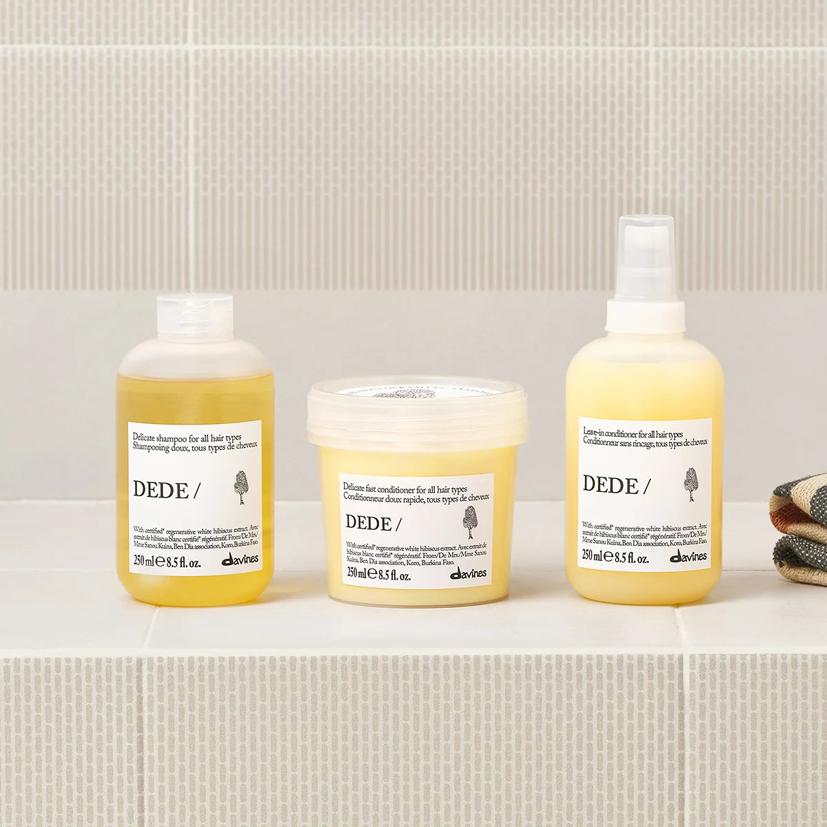 Three bottles of Dede hair care products on a bathroom shelf with a tiled wall background.