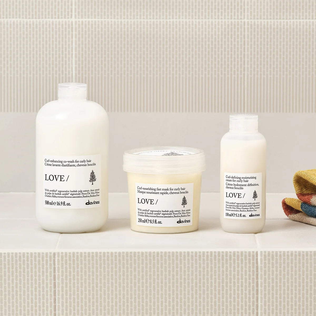 Three Davines hair care products on a bathroom shelf with a tiled wall background.