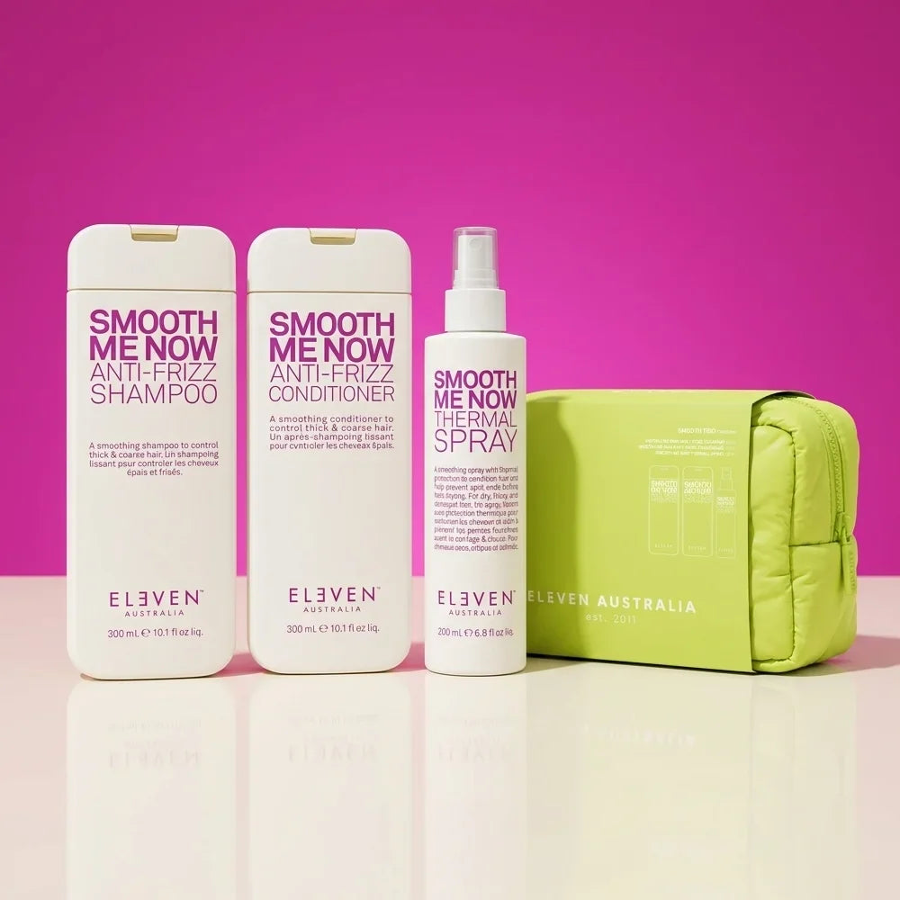 Set of 'Eleven Australia' hair care products including shampoo, conditioner, thermal spray, and pouch on a pink background. Holiday Smooth Gigt Set