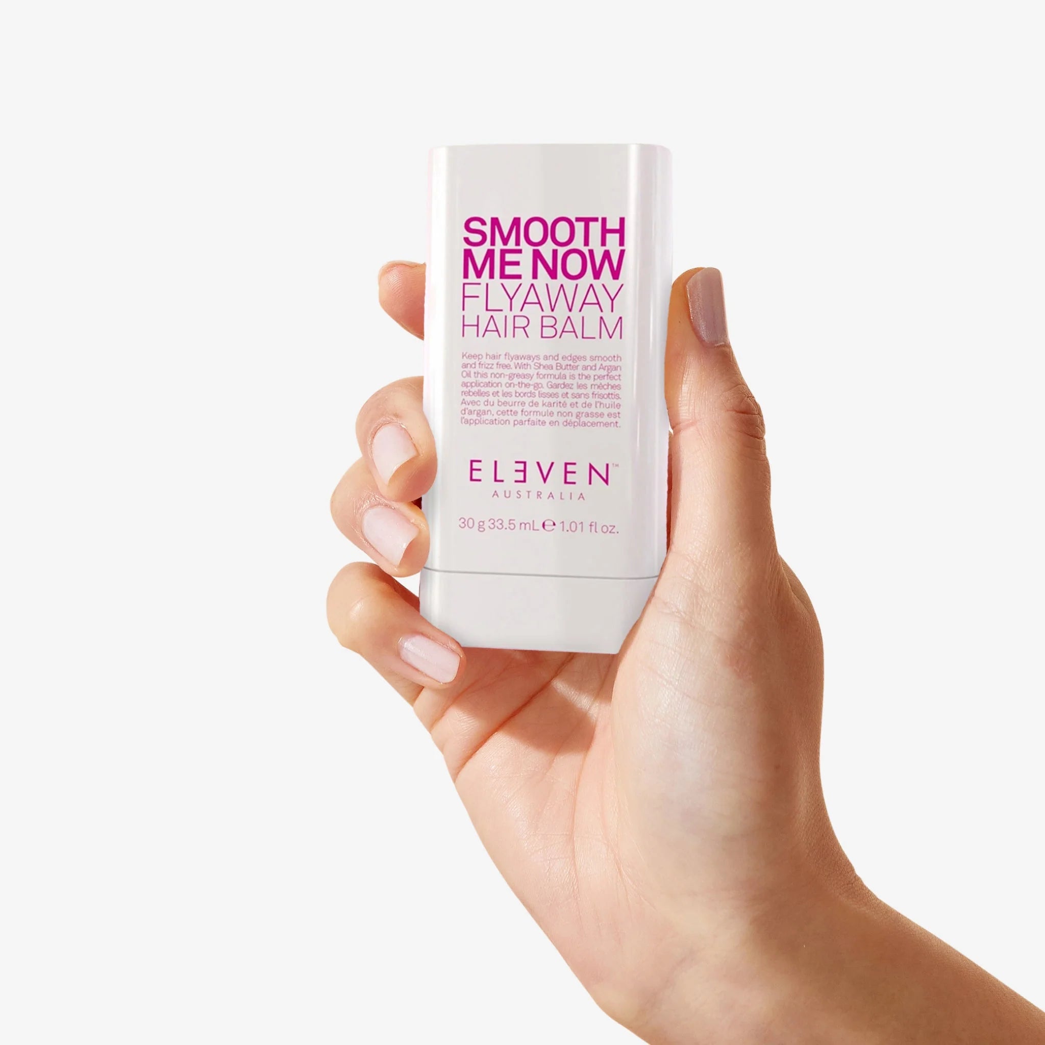 Hand holding a 'Smooth Me Now Flyaway Hair Balm' by Eleven Australia against a white background