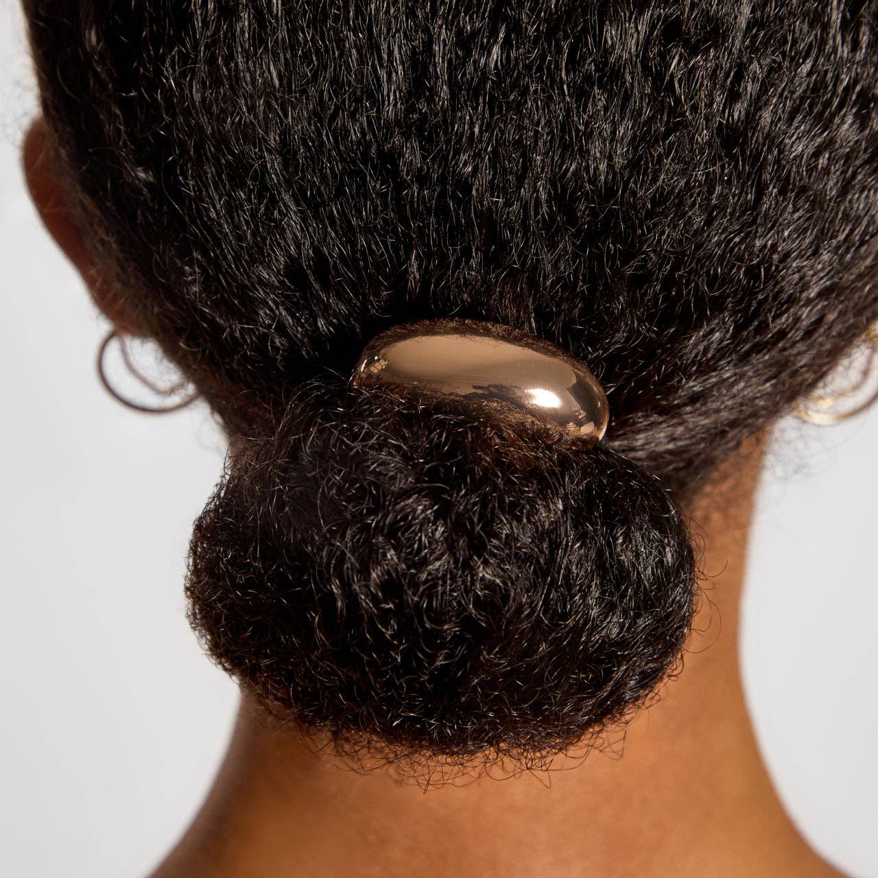 Close-up of a person's hair bun with a hair tie against a white background. Kitsch gold metal cloud cuff ponitail holder
