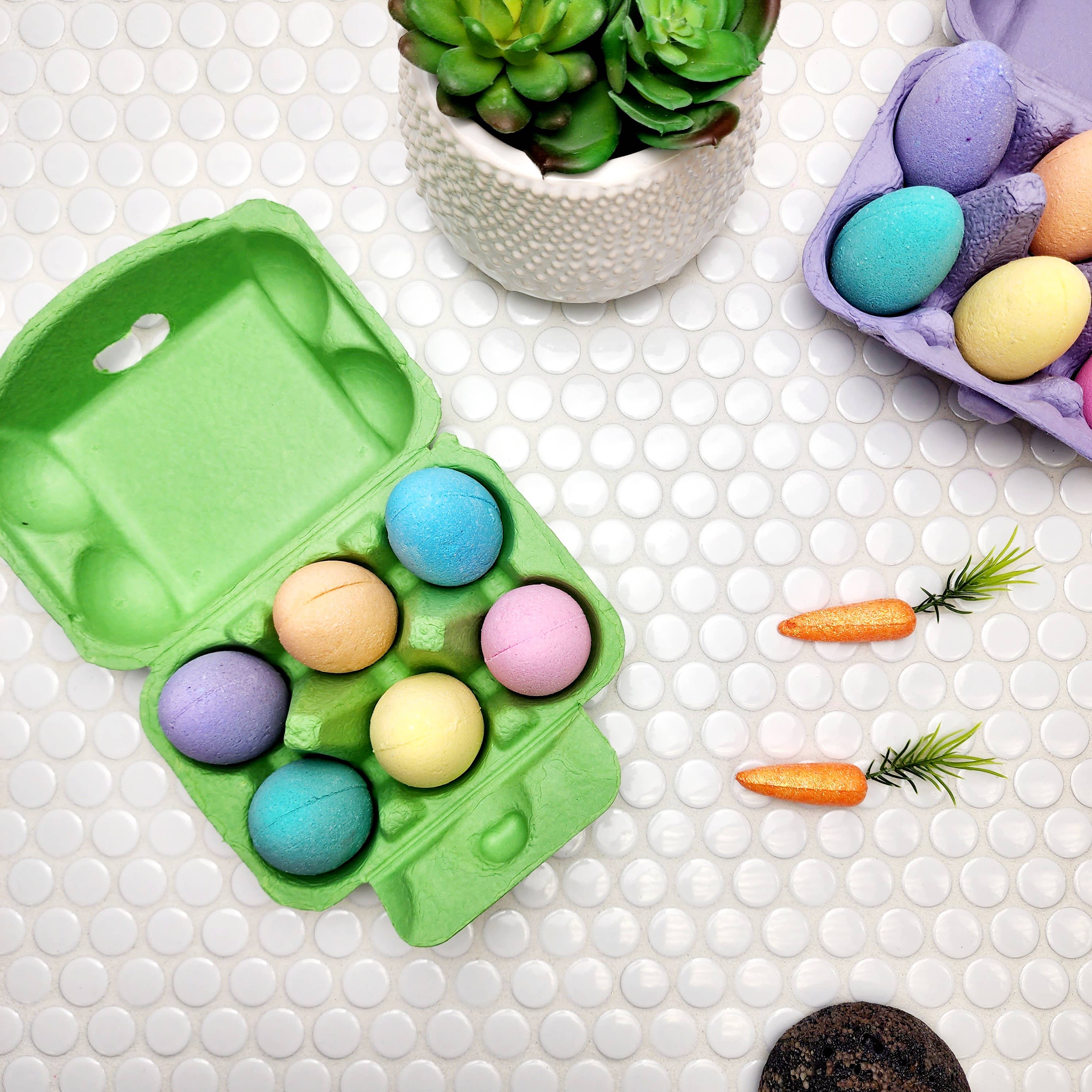 Happy Hippo Colorful Easter egg bath bombs in a green holder on a textured white surface with decorative carrots and plants.