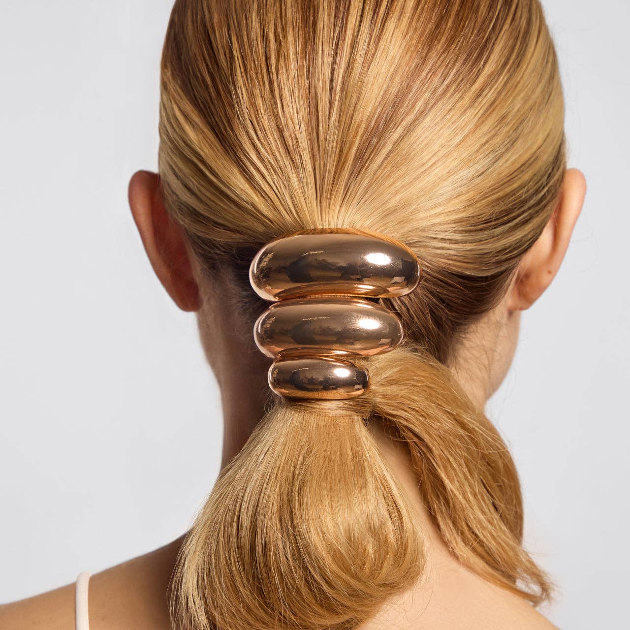 Gold hair tie on a person's ponytail against a plain background. Kitsch gold metal cloud cuff ponitail holder