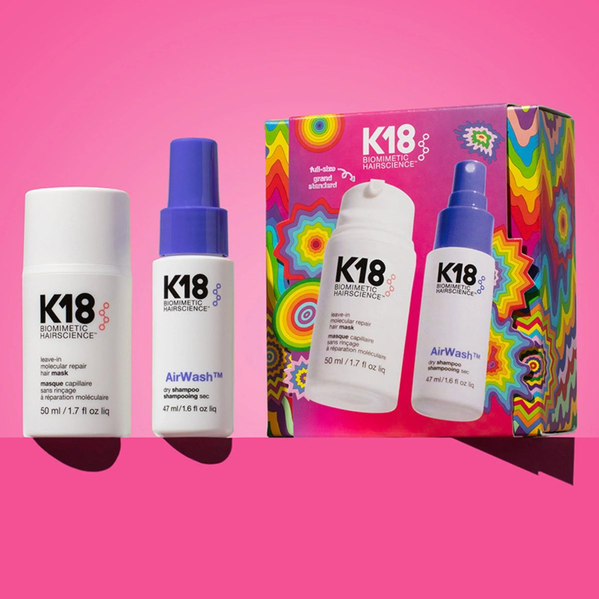 Three K18 Cosmetics haircare products and their packaging displayed against a bright pink background. The set includes a white bottle labeled Wash-01, a white bottle with a blue cap labeled AirWash, and a colorful box featuring the K18 brand and psychedelic swirl patterns.