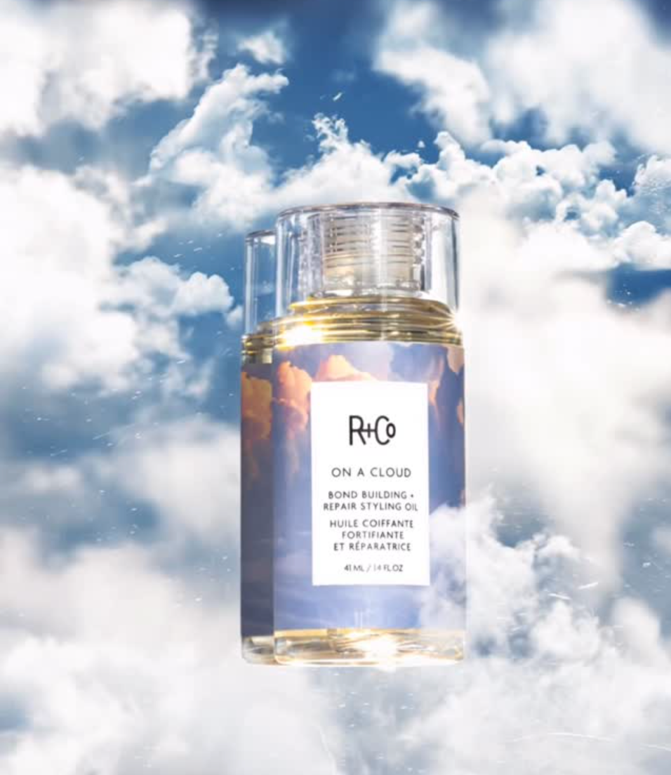 R+Co On a Cloud Repair Oil hair product bottle with clouds in the background