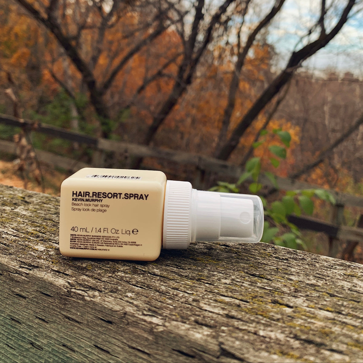 Hair resort spray bottle with beige label on a wooden surface with autumn trees in the background